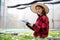 Asian woman farmer using tablet and notebook for inspecting the quality of organic vegetables grown using hydroponics