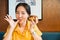 Asian woman is finger-licking good while having a chocolate glazed homemade donut topping with crush hazelnut in a modern cafe.