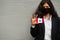 Asian woman at formal wear and black protect face mask hold Austral Islands flag at hand against gray background. Coronavirus at