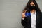 Asian woman at formal wear and black protect face mask hold Chuuk State flag at hand against gray background. Coronavirus at