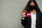 Asian woman at formal wear and black protect face mask hold Tuamotus flag at hand against gray background. Coronavirus at country