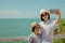 Asian woman and girl standing relax on cliff nearly seashore, They taking selfie together.