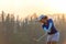 Asian woman golf player doing golf swing tee off on the green sunset evening time,