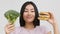 Asian Woman Holding Burger And Broccoli Choosing Food, White Background