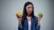 Asian woman holding sweet greasy donut and juicy green apple in hands, decision