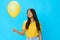 Asian woman holding a yellow balloon on a blue background in a yellow T-shirt smile with teeth, cute woman, copy space