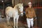 Asian woman horse breeder leading white thoroughbred racehorse in stable