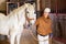 Asian woman horse breeder leading white thoroughbred racehorse in stable