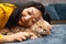 Asian woman lie near her orange cat also scratch the chin of cat to make it relax and happy on bed.