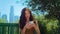 Asian woman looking back on blurred cityscape holding smartphone in park closeup