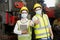 Asian woman and man wearing a mask holding a tablet and show thumb up in an industrial factory. Professional technicians are holdi