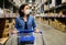 Asian woman in a medical mask with shopping cart in a warehouse