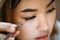 Asian woman placing decorative eyelashes on eye