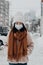 Asian woman in a protective mask walking along a snowy street. Girl in a mask on a background of skyscrapers in winter. The