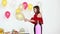 Asian woman in red shirt using balloon pump to blowing glitter balloon, colorful balloons behind her, concept for party.