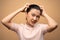 Asian woman scratching her head standing isolated on beige background