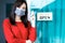 Asian woman shop owner smiling wearing medical face mask hanging label `Welcom we are open` and showing alcohol bottle. She open