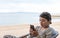 Asian woman sitting at the beach closely looking at her cell phone reading and looking focused