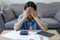 Asian woman sitting covering face with hands with many bills on table at home. she feels stressed. Debt or bankruptcy concept