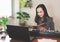 Asian woman  sitting with electric piano, writing on notebook looking at computer notebook on table. Teaching or learning piano