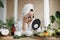 Asian woman sitting at table in white towel and bathrobe, looking at mirror and applying patches