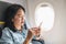 Asian Woman sitting at window seat in airplane and turn on airplane mode on mobile phone before take off