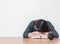 Asian woman sleep by lied on desk after she tired from reading book on blurred brown wooden desk and white cement wall textured ba