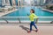 Asian woman in sportswear runs along the Dubai Marina embankment with a smartphone and headphones. Fitness classes and