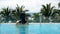 Asian woman springs up from under the pool, swimming and relax at the pool with palm tree tropical beach at background.