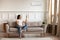 Asian woman switching on air conditioner while resting seated indoors