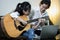 Asian woman teaching child girl to play guitar, student learning how to play the guitar with the help of a teacher, happy daughter