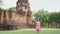 Asian woman tourist in pink dress with medical face mask at `Muang Singha` ancient ruin temple in Kanchanaburi, Thailand. new norm