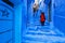 Asian woman tourist in red dress walking on a street in Medina of Chefchaouen