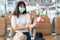 Asian woman tourist wearing mask looking happy while smiling behind the mask and sitting social distancing chair in airport