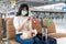 Asian woman tourist wearing mask using mobile phone searching airline flight status and sitting social distancing chair in airport