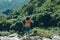 Asian woman traveler standing on rock and arms up in the air at landscape view of green rain forest and stream water in sunny day