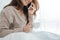 Asian woman using the smartphone on her bed while holding cup of coffee in the morning.