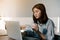 Asian woman Wearing a blue striped shirt sitting in front of a laptop computer And in the hand holding a cup of coffee With the