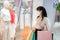 Asian woman wearing mask over her face looking new collection dress at shopping mall with shopping bag for healthcare and