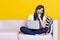 Asian woman wearing medical mask and working from home use laptop computer while sitting on sofa over isolate yellow background