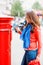 Asian woman wearing, sunglasses, red coat, blue scarf, jeans and white shirt putting card to red postbox and walking around Engl
