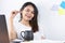 Asian woman wearing a white T-shirt The hand is holding the glasses Working at home And on the desk, there is a black coffee mug