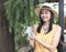 Asian woman  wearing yellow sleeveless shirt, hat ,standing in the garden, holding plant pot of Black Gold Philodendron. summer