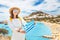 Asian woman in white dress posing with greek flag in front of the famous Lindos town on Rhodes island. Vacation and travel