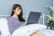 Asian woman working on bed .She dress sweater violet colour.Morning check email internet from notebook
