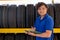 Asian worker or employee of auto parts shop hold the document and stand in front of tires on shelves and look to camera with