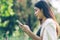 Asian working woman texting at smartphone while sitting on bench in the public park