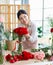 Asian young cheerful professional female flower shopkeeper decorator florist wearing apron standing smiling holding decorating red