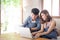 Asian young couple using laptop computer think and searching internet together, man and woman casual smiling work at home