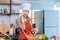 Asian young female chef housewife wears white tall cook hat and apron standing smiling on smartphone call holding wooden spoon